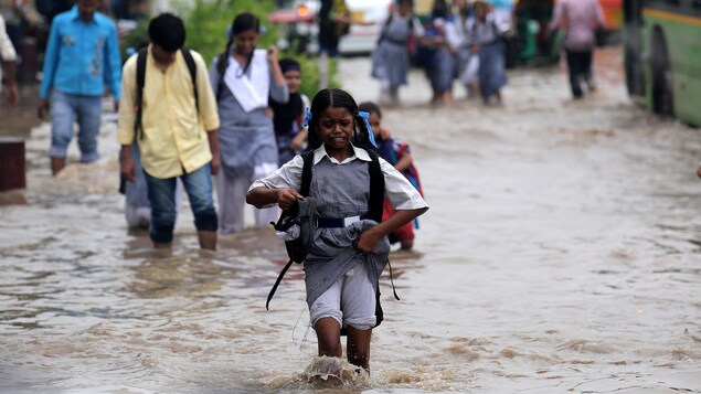 Une fillette avance dans la rue inondée, ses souliers à la main et une grimace au visage.