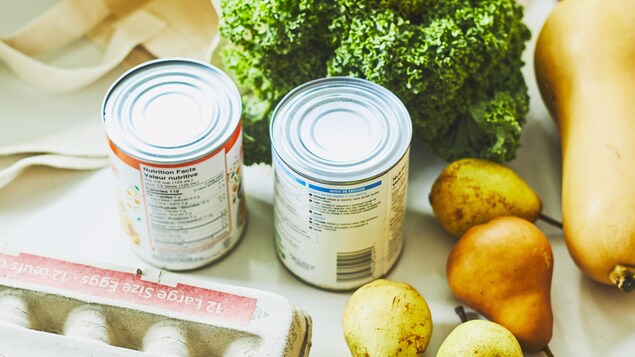 Sur un comptoir de cuisine sont déposés plusieurs aliments comme des œufs, du brocoli, des poires et des légumineuses en cannes.