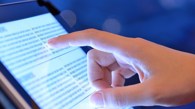 Un doigt pointe un article affiché sur l'écran d'une tablette.