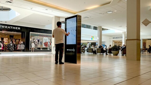 Un visiteur tape sur l'écran d'orientation tactile avec son doigt dans un centre commercial.