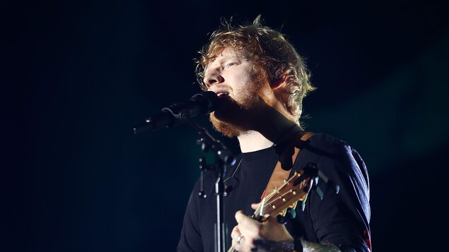 Ed Sheeran joue de la guitare sur scène et chante dans un microphone.