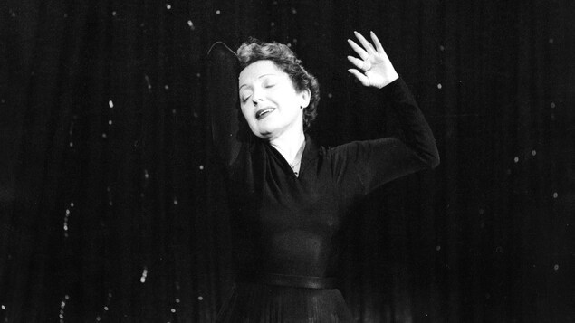 La chanteuse Édith Piaf, en performance, les yeux fermés dans une pose dramatique.