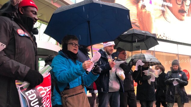 Une dizaine de personnes sous la pluie chantent en lisant un papier.