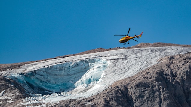 Un hélicoptère transportant des secouristes survole le glacier.