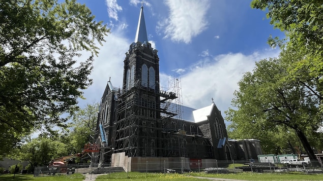 Une église flanquée d'échafauds sur un terrain bordé d'arbres matures.