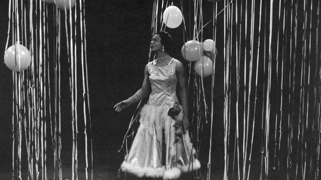 Eleanor Collins chante sur une scène décorée de guirlandes et ballons.