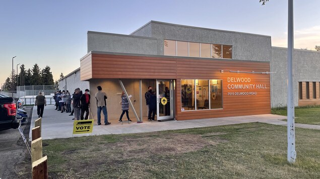 Des gens en file devant le bureau de vote alors que le soleil se couche.