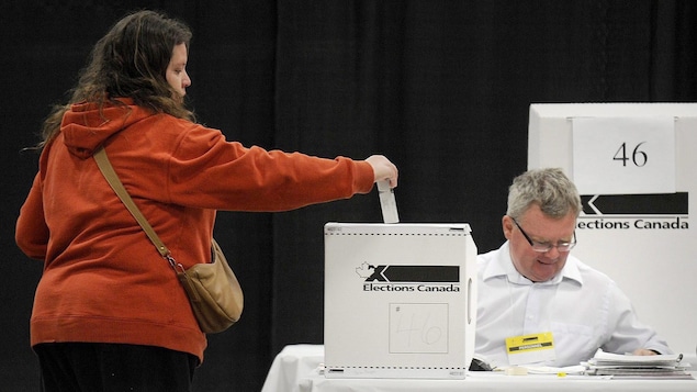 Une femme glisse son bulletin de vote dans une boîte de scrutin ornée du logo d'Élections Canada.