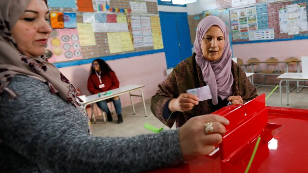 Une Tunisienne s'apprête à déposer son bulletin de vote dans une urne sous le regard d'une scrutatrice.