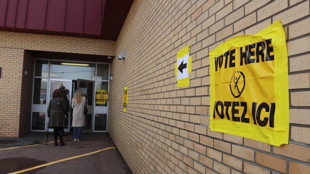 Une affiche jaune sur un mur indique la direction du bureau de vote.
