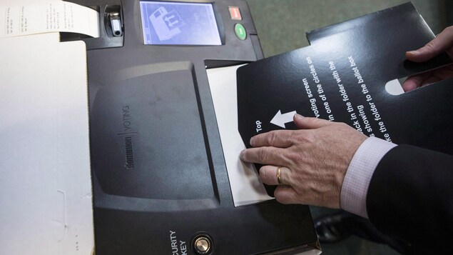 Un homme glisse un bulletin dans une tabulatrice de vote. Un homme glisse un bulletin dans une tabulatrice de vote.