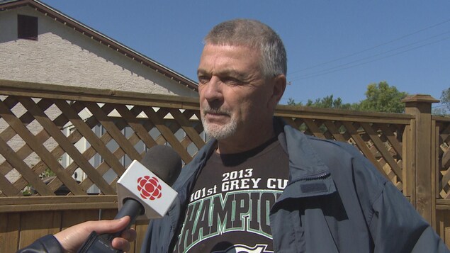 M. Robinson écoute attentivement la journaliste poser sa question. Il porte un chandail noir de l'équipe de football saskatchewanaise, les Roughriders. M. Robinson écoute attentivement la journaliste poser sa question. Il porte un chandail noir de l'équipe de football saskatchewanaise, les Roughriders.