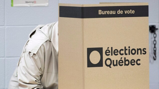 Un électeur se trouve derrière un isoloir en carton.