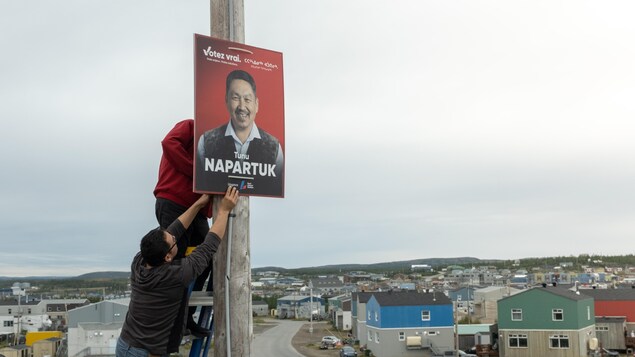 Des hommes installent une affiche de Tunu Napartuk sur un poteau.