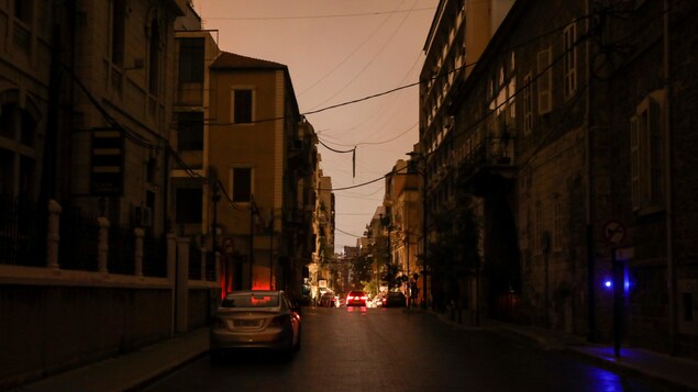 Une rue éclairée seulement par les phares d'une voiture.