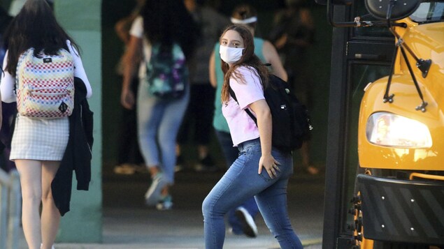 Une élève du secondaire qui porte un masque descend de l'autobus scolaire.