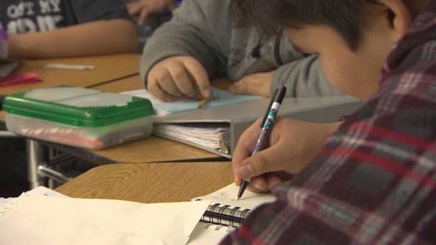 Un élève autochtone écrit dans son carnet d'école
