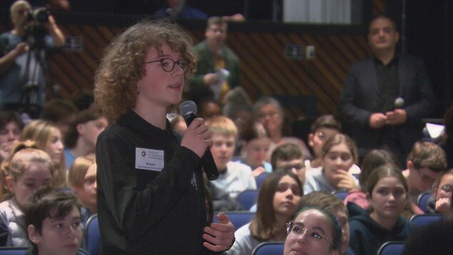 Un jeune avec un micro dans les mains, debout dans l'auditorium.