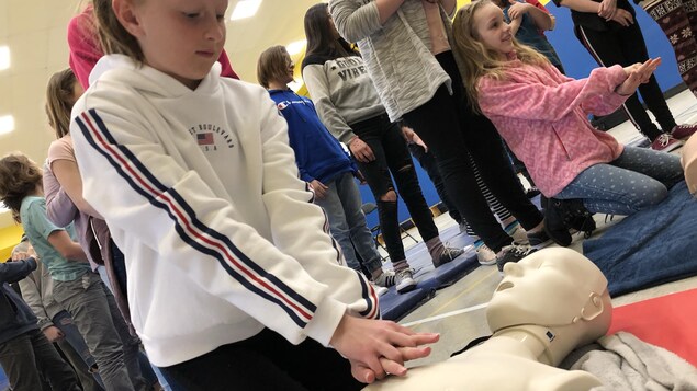 Une élève est penchée sur un mannequin pour pratiquer un massage cardiaque.