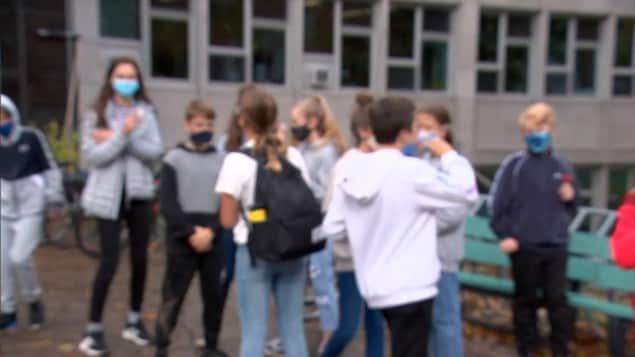 Une image floue d'élèves devant un bâtiment. Ils portent leur masque.