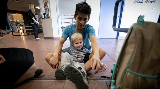 Eli Gooding est assis entre les jambes d'un homme adulte.