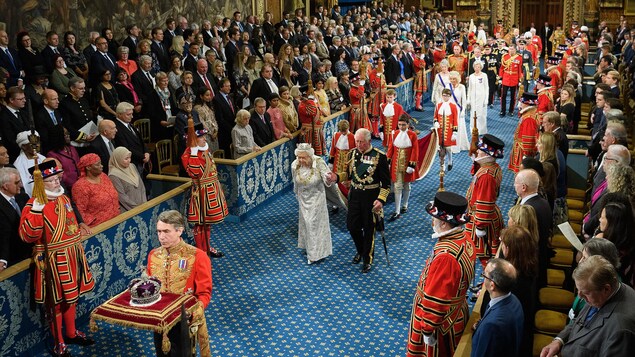 La reine, qui porte une couronne, marche en tenant la main de son fils.