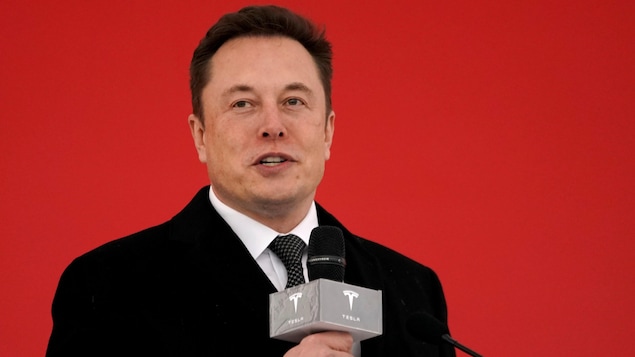 Elon Musk parle au micro devant un mur rouge.