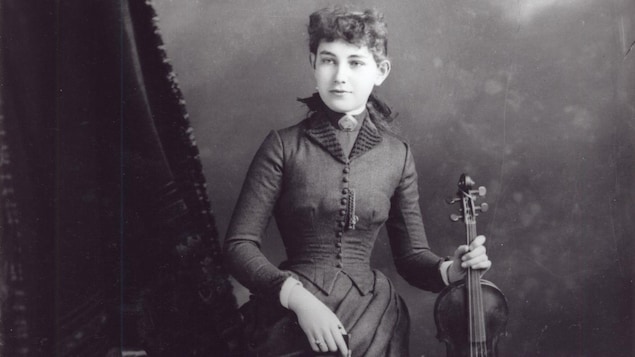 La jeune femme sourit en posant avec son violon dans un studio de photographe.