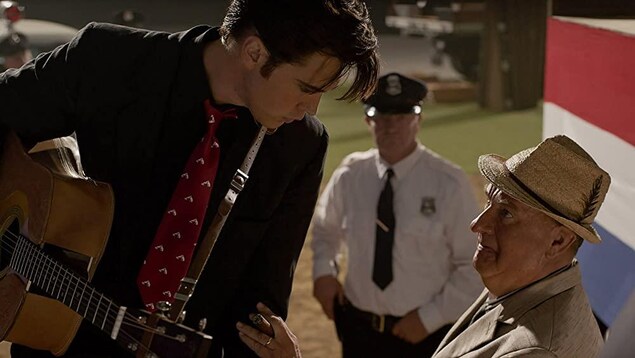 Austin Butler, incarnant Elvis Presley, regarde son gérant, joué par Tom Hanks, alors qu'il a une guitare au cou.