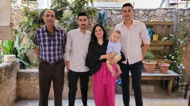 A woman holding a baby poses for a picture with an elderly man and two young men for a picture in a garden.