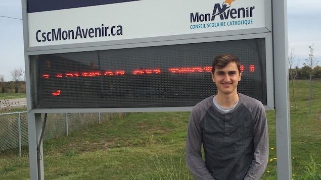 Photo d'Émile Bélanger devant le panneau de l'école Photo d'Émile Bélanger devant le panneau de l'école