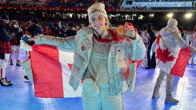 Emily Clark porte sa médaille d'or et tient un drapeau canadien lors de la cérémonie de clôture des Jeux olympiques de Beijing.