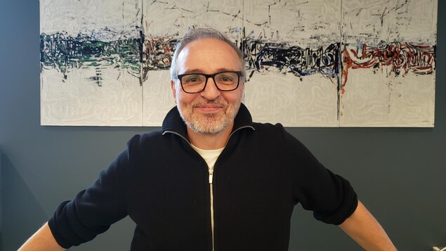un homme qui sourit devant un tableau.