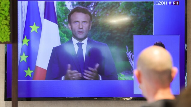 Un homme regarde une télévision où Emmanuel Macron prononce un discours.