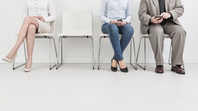 Trois personnes sont assises sur des chaises enlignées contre un mur.