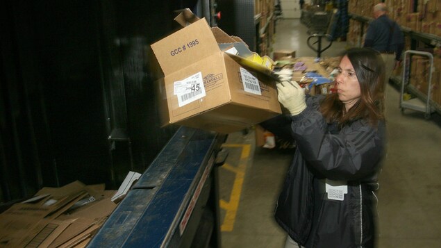 Photo d'une femme qui dépose une boîte dans une benne de recyclage dans un entrepôt. Photo d'une femme qui dépose une boîte dans une benne de recyclage dans un entrepôt.