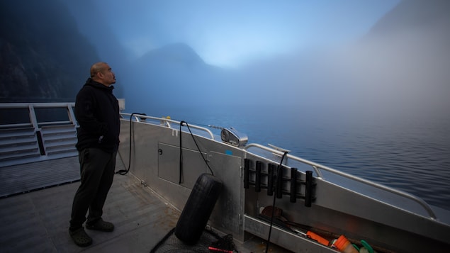 Douglas Neasloss sur le pont d'un bateau dans un fjord embrumé, près de Klemtu, en Colombie-Britannique, en octobre 2023.