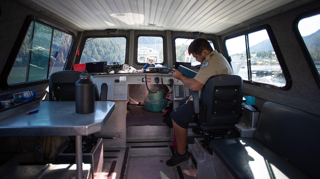 Medrick Robinson dans la cabine d'un bateau, en train de regarder un registre, à Klemtu, en Colombie-Britannique, en octobre 2023.