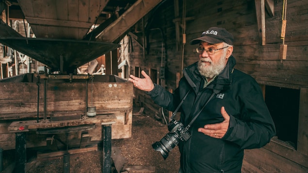 Gordon Goldsborough est dans un très vieil élévateur à grains tout en bois, son appareil photo autour du coup, à Barnsley au Manitoba, début juin 2022.