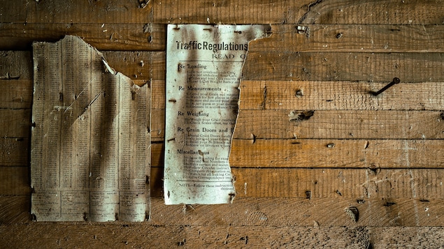 Un mur en bois avec deux vieilles affiches jaunies par le temps, à Barnsley au Manitoba, début juin 2022.