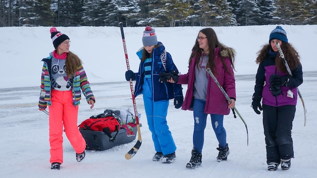 Quatre filles transportent de l'équipement de hockey.