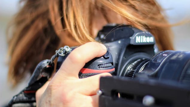 Une femme tient une caméra Nikon devant son visage.