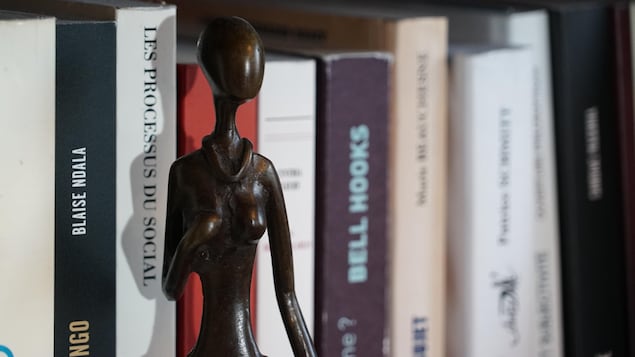Une sculpture africaine en bois qui est un personnage féminin devant une étagère de livres.