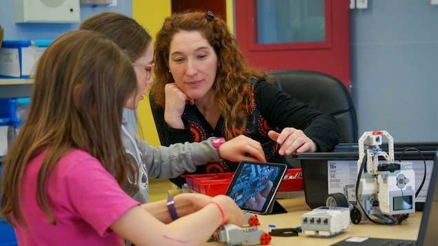 Karine Dubé aide deux élèves à fabriquer un robot.