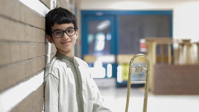 Omar pose avec son trombone dans les corridors de Sistema à Moncton.