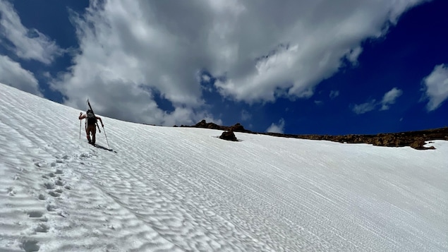 Au loin, un skieur alpin qui fait l'ascension d'une montagne enneigée.