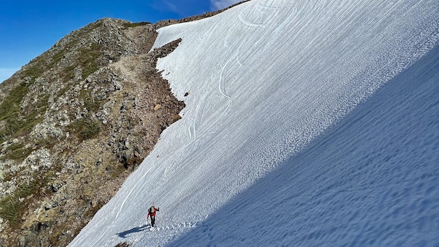 Au loin, un skieur alpin sur une montagne partiellement enneigée.