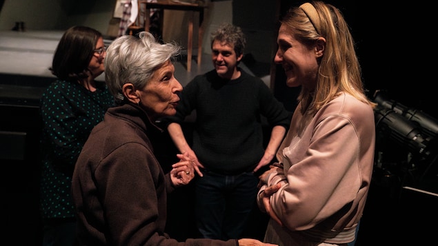 Deux femmes discutent ensemble devant une scène de théâtre et un homme et une femme discute derrière elles.