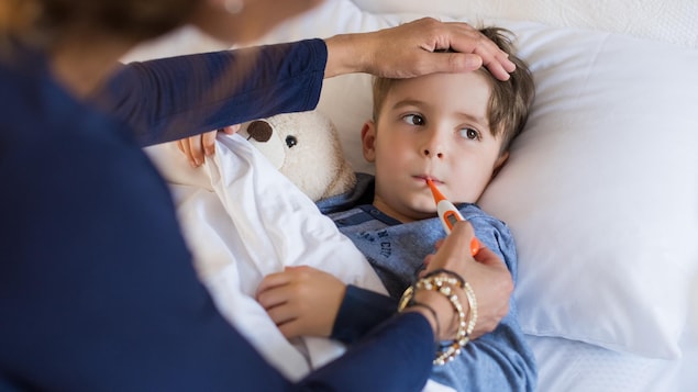 A person takes a sick child's temperature with a thermometer.