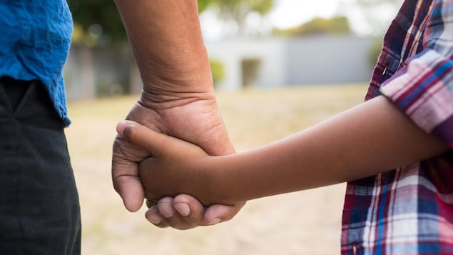La main d'un adulte tient celle d'un enfant.